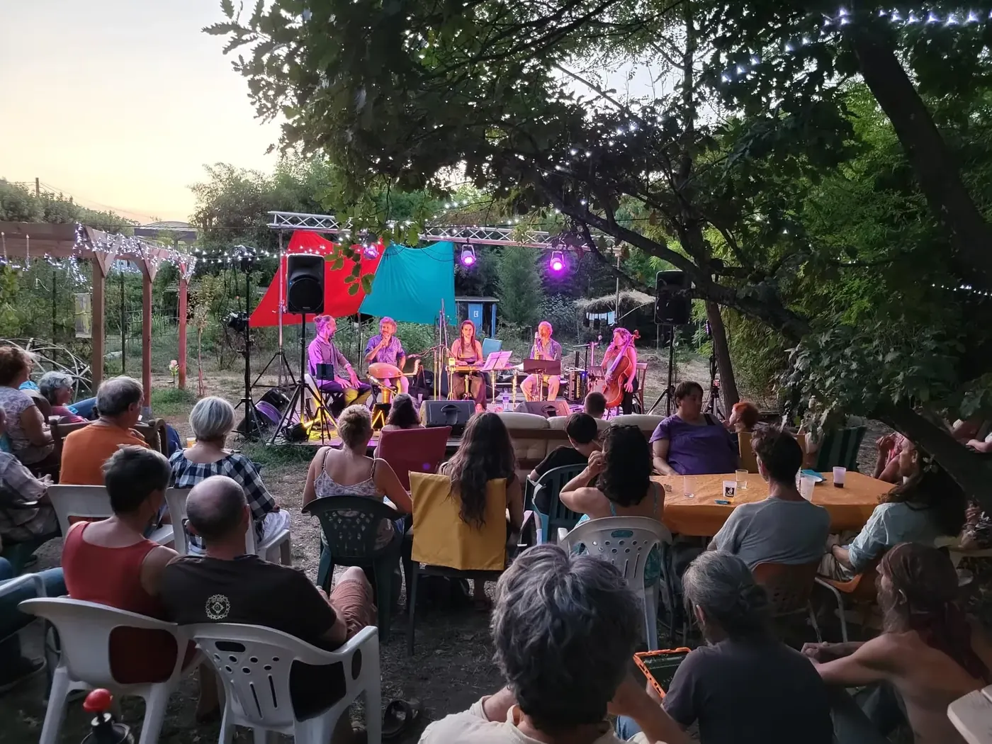 Concert au couchant sur la scène de plein air, public installé sous les guirlandes